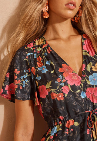 a-close-up-shot-of-a-woman-modelling-a-short-sleeve-floral-mini-dress-with-a-lace-hem-standing-against-a-textured-beige-wall