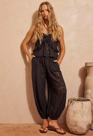 a-woman-modeling-a-black-lace-sleeveless-top-and-matching-black-lace-harem-pants-standing-in-a-warm-beige-studio-setting-with-decorative-ceramic-pots
