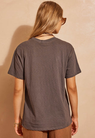 styled with brown pants and sunglasses against a beige wall.